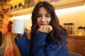 Cute young caucasian girl with wavy hair holds cup of cappuccino looking at camera with smile. Royalty Free Stock Photo