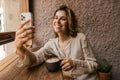 Cute young caucasian woman communicates by video via smartphone sitting in cafe. Royalty Free Stock Photo