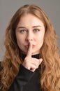 Cute young Caucasian woman touches her lips with her index finger making a silence gesture. Looking into the camera. Front view Royalty Free Stock Photo