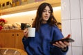 Cute young caucasian woman uses her smartphone spends free time in cafe during winter morning.