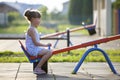 Cute young child girl outdoors on see-saw swing on sunny summer day