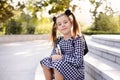 Cute young child girl 5-6 year old wear checkered black and white dress and backpack holding books sitting on stairs outdoors clos Royalty Free Stock Photo