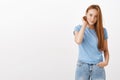 Cute young european redhead female student with freckles flicking hair behind ear holding hand in pocket and gazing with Royalty Free Stock Photo