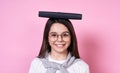 Cute young funny girl in glasses holds books on her head on a pink background Royalty Free Stock Photo