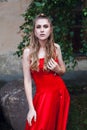 Young girl with blond flowing long hair and beautiful make-up, in a long red dress, stands on the street Royalty Free Stock Photo