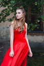 A cute young girl with blond flowing long hair and beautiful make-up, in a red dress, stands on the street Royalty Free Stock Photo