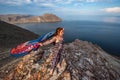 A cute young girl in a dress with a colorful scarf fluttering behind stands on a rock above Lake Baikal. Royalty Free Stock Photo