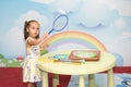 A cute young girl in a dress makes soap bubbles in the children`s room. Royalty Free Stock Photo