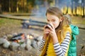 Cute young girl drinking tea and roasting marshmallows on stick at bonfire. Child having fun at camp fire. Camping with children Royalty Free Stock Photo