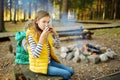 Cute young girl drinking tea and roasting marshmallows on stick at bonfire. Child having fun at camp fire. Camping with children Royalty Free Stock Photo