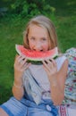 Cute young girl eating water-melon on the grass in summertime