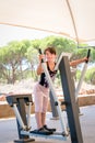 Cute young girl exercising arms and chest on cross trainer gym machine outdoors. Royalty Free Stock Photo