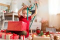Cute young girl opening large red christmas present while sitting on living room floor. Candid family christmas time. Royalty Free Stock Photo