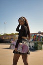 Cute young girl with punk style and heterochromia holding a skateboard in her hand looking flirtatiously at the camera in a Royalty Free Stock Photo