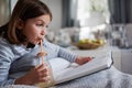 Cute young girl reading exciting book and drinking lemonade at home Royalty Free Stock Photo