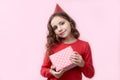 Cute young girl in red birthday cap holds before her a gift box with happy joyful expression and smile Royalty Free Stock Photo