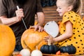 Cute young girl sitting on kitchen table, helping her father to carve large pumpkin. Halloween family lifestyle. Royalty Free Stock Photo