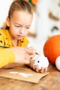 Cute young girl sitting at a table, decorating little white pumpkins with her mother. DIY Halloween holiday and family lifestyle. Royalty Free Stock Photo