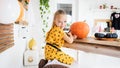 Cute young girl sitting at a table in living room, drawing a face on a large halloween pumpkin, looking at camera and smiling.