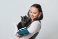 Cute young girl student with a funny cat in her arms reading a book. On light background Royalty Free Stock Photo