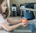 Cute young girl washing and sanitizing fresh fruit. Wash food. Child hands holding tasty apple under running water in kitchen sink