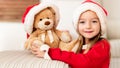 Cute young girl wearing santa hat hugging her christmas present, soft toy teddy bear. Happy kid with xmas present, smiling. Royalty Free Stock Photo