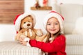 Cute young girl wearing santa hat holding her christmas present, soft toy teddy bear. Happy kid with xmas present, smiling. Royalty Free Stock Photo