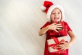 Cute young girl wearing santa hat lying on the floor, holding christmas presents and laughing at camera. Happy kid at christmas. Royalty Free Stock Photo