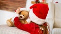 Cute young girl wearing santa hat playing with her christmas present, soft toy teddy bear. Happy kid with xmas present. Royalty Free Stock Photo