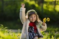 Cute young girl wearing wreath of dandelions and smiling while sitting on grass in park Royalty Free Stock Photo
