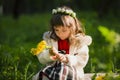 Cute young girl wearing wreath of dandelions and smiling while sitting on grass in park Royalty Free Stock Photo