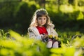 Cute young girl wearing wreath of dandelions and smiling while sitting on grass in park Royalty Free Stock Photo