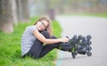 Cute young going rollerblading sitting in grass putting on inline skates