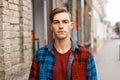 Cute young handsome man with a stylish hairstyle in a trendy T-shirt in a fashionable plaid shirt walks in the city