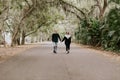 Cute Young Happy Loving Couple Walking Down an Old Abandoned Road with Mossy Oak Trees Overhanging Royalty Free Stock Photo