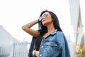 Cute young hipster woman in fashionable sunglasses in a trendy black t-shirt in a stylish denim jacket straightens hair. Royalty Free Stock Photo