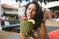 Cute young latino woman drinking cocktail from fresh pineapple ananas during summer with summer outfit at a lounge bar outdoor Royalty Free Stock Photo