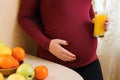 Cute young pregnant woman with glass of fresh juice. Pregnant woman on kitchen with healthy food