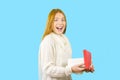 Cute young red-haired girl, with an open box with a gift, smiles with an open mouth and looks into the camera, isolated Royalty Free Stock Photo