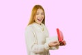 Cute young red-haired girl standing in profile with an open box with a gift smiles with an open mouth and looks into the