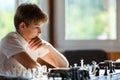 Cute young smart boy in plays chess on the training before the tournament. Hand makes a move on chessboard. Chess summer camp. Royalty Free Stock Photo