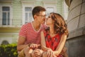 Cute young smiling couple in love touching noses, hugging, sitting outdoors at green city street, summertime