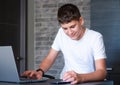 Cute young teenager in white shirt sitting behind desk in kitchen next to laptop and study. Royalty Free Stock Photo