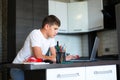 Cute young teenager in white shirt sitting behind desk in kitchen next to laptop and study. Royalty Free Stock Photo