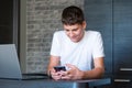 Cute young teenager in a white shirt sitting behind a desk in the kitchen next to laptop and study. Serious boy makes homework Royalty Free Stock Photo