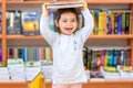 Cute Young Toddler Standing and Holding Book in Head. Child in a Library, Shop,Bookstore. Royalty Free Stock Photo