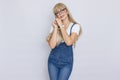 Cute young woman blonde with long hair in a denim jumpsuit and glasses. The girl has a white watch on her hand. Royalty Free Stock Photo