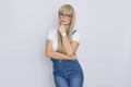 Cute young woman blonde with long hair in a denim jumpsuit and glasses. The girl has a white watch on her hand. She posing over Royalty Free Stock Photo