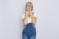 Cute young woman blonde with long hair in a denim jumpsuit and glasses. The girl has a white watch on her hand. She posing over Royalty Free Stock Photo