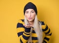 Cute young woman blows a kiss to you from his palm, model wearing woolen cap and sweater,  on yellow background. Love Royalty Free Stock Photo